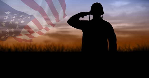 Silhouette of a soldier against a sunset sky with a waving American flag